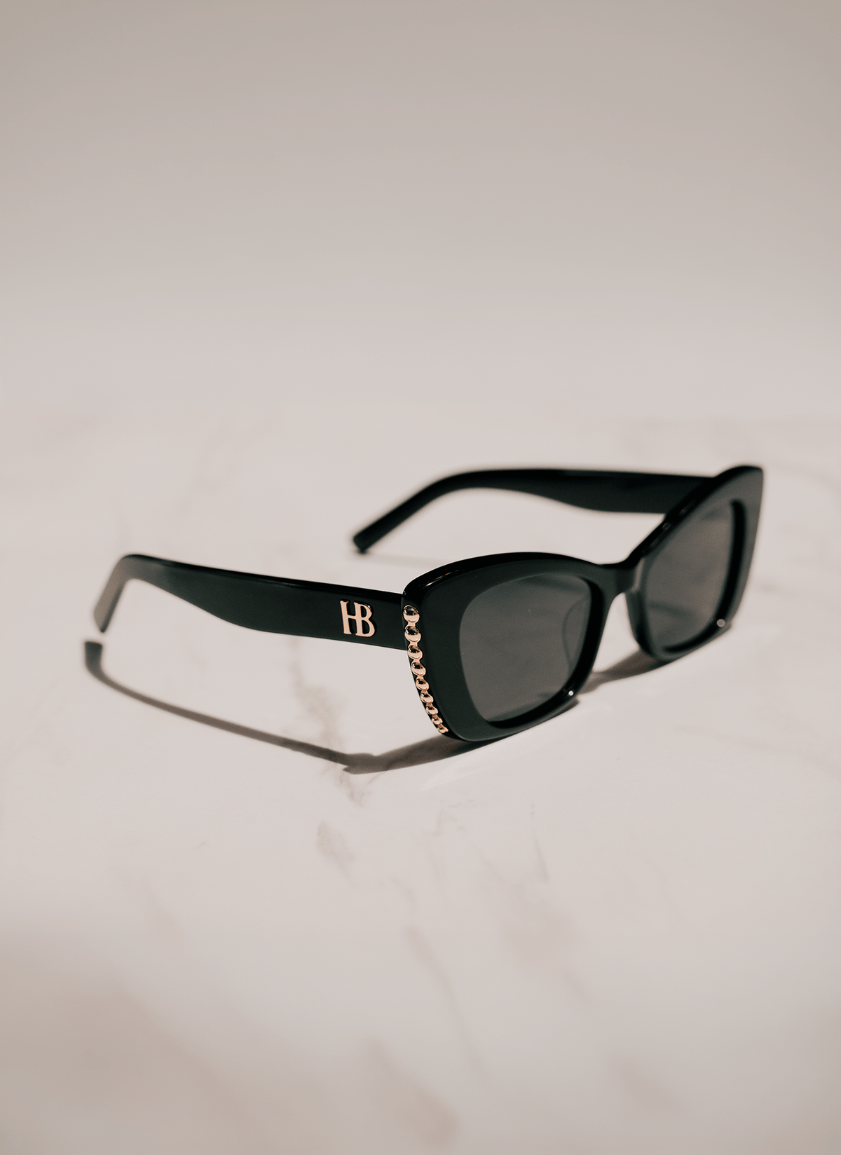Black cat-eye sunglasses with dark lenses, featuring a gold &