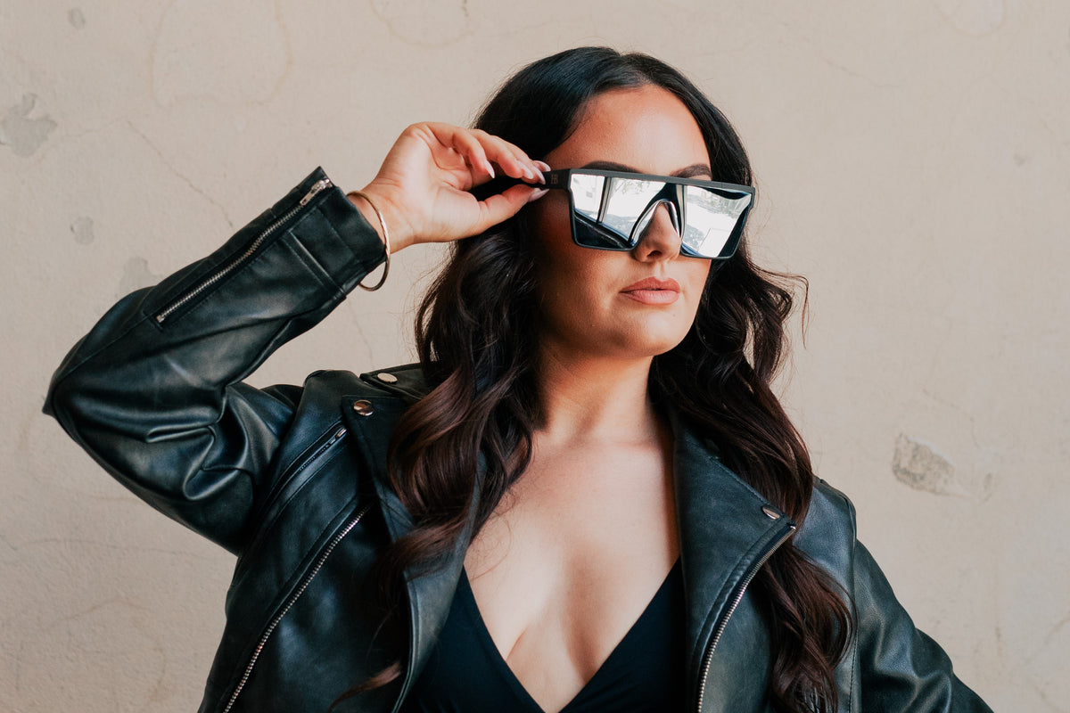 Woman wearing a black leather jacket and reflective sunglasses against a neutral background