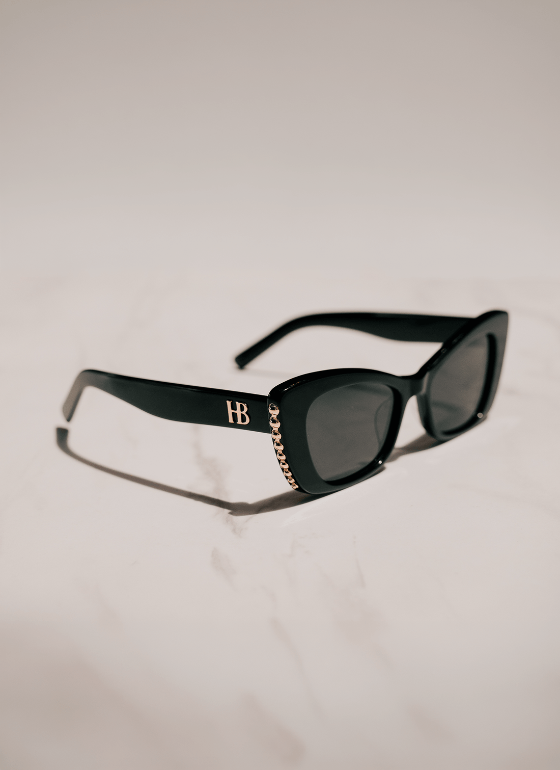 Black cat-eye sunglasses with dark lenses, featuring a gold &