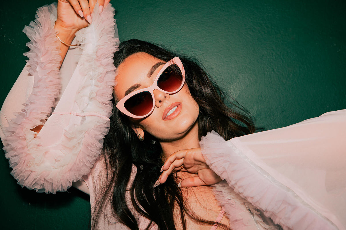 Woman wearing pink sunglasses and a light pink outfit against a green background